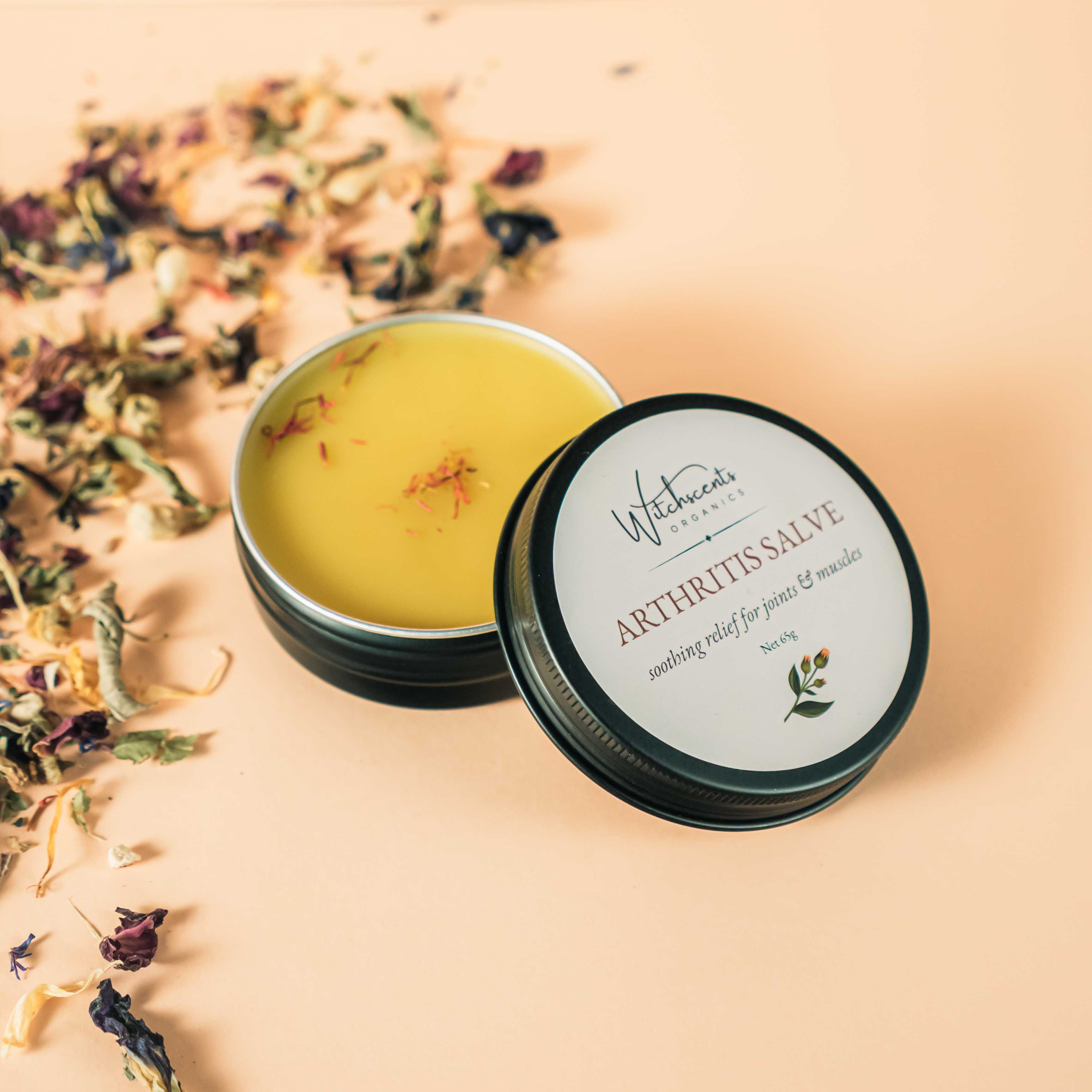 Open tin of arthritis salve with a label on a beige background with dried herbs.